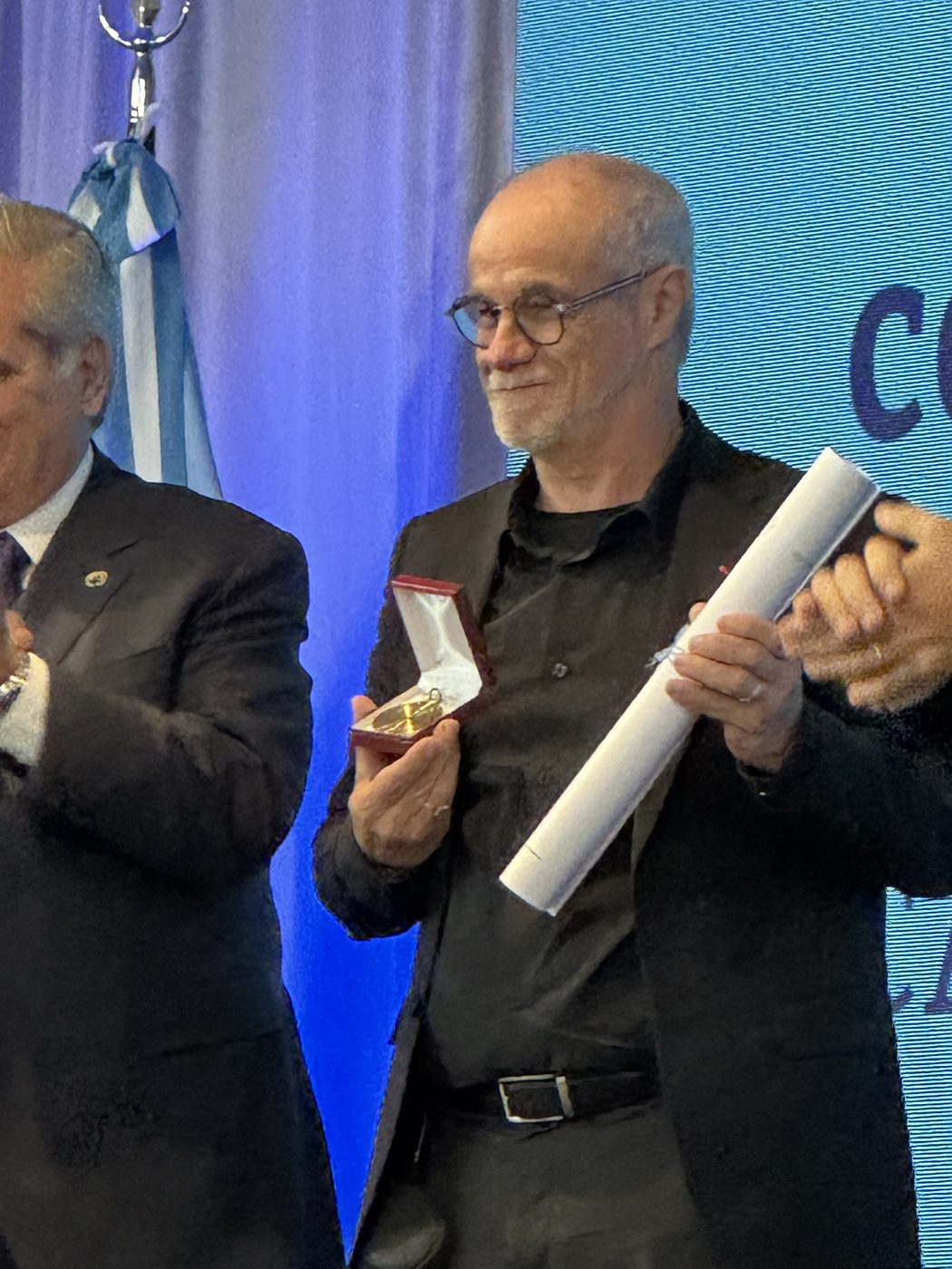 Carlos Moreno holding the Universidad de Buenos Aires Honorary Doctorate medal in its case and the rolled diploma, applauded on stage beside the Argentine flag at the V Congreso Internacional de Ciudades Inteligentes