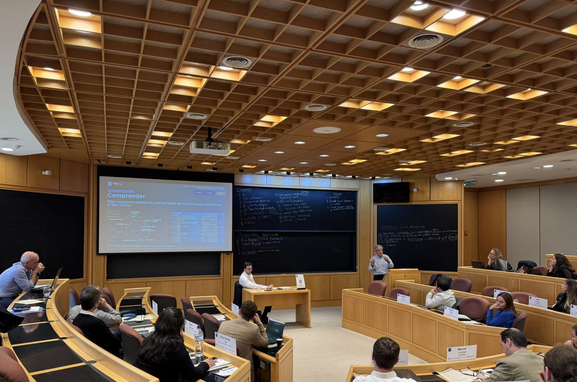 A speaker presenting the slide Ecosistema de Innovacion de Buenos Aires, tres nodos que conectan talento, empresas y conocimiento, to seated participants in a tiered classroom at IAE Business School