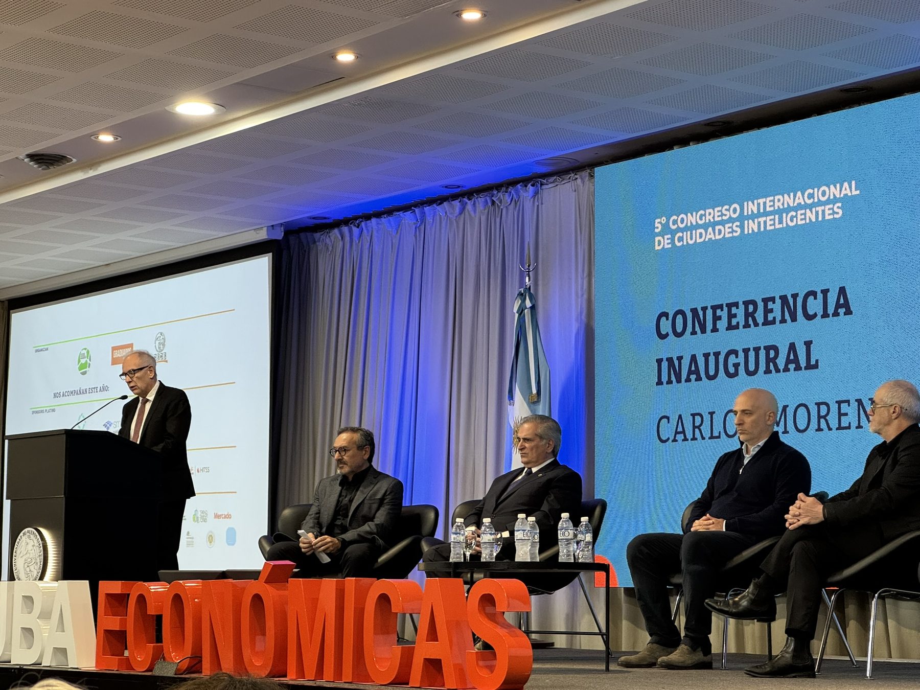 The stage of the V Congreso Internacional de Ciudades Inteligentes at UBA Economicas, with a speaker at the lectern, four seated participants and a screen reading Conferencia Inaugural Carlos Moreno